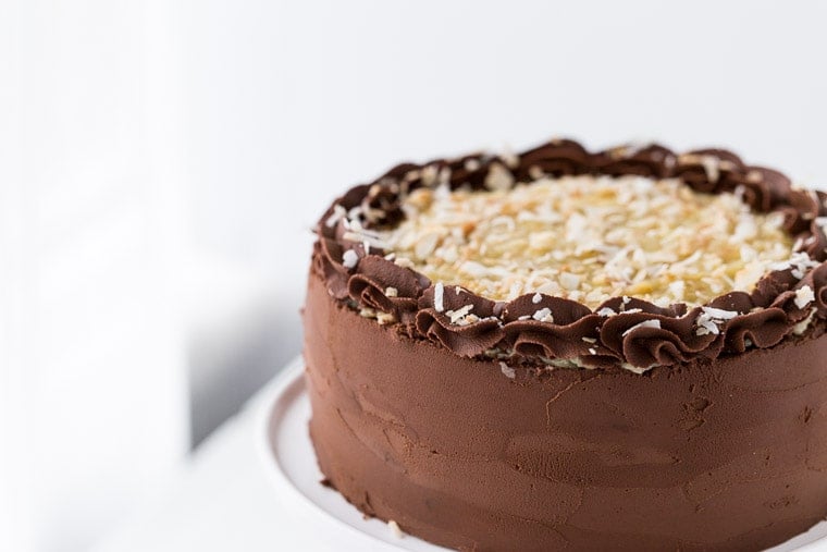 This German Chocolate Cake is four layers of moist chocolate cake soaked in rum syrup and filled with sweet coconut custard filling and wrapped beautifully in a chocolate ganache frosting.